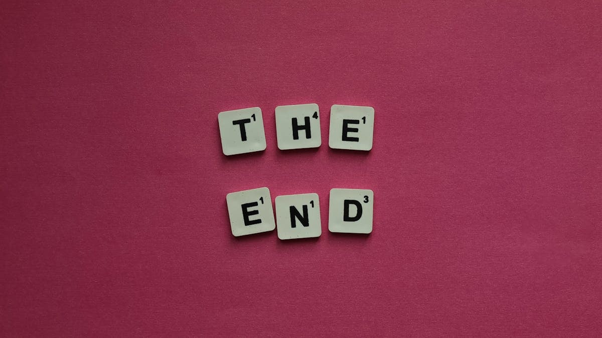 Scrabble tiles spell 'The End' against a vibrant pink background, symbolizing conclusion.
